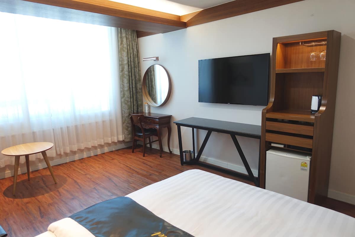 A hotel room with a bed, a desk, a chair, a television, a small refrigerator, and a wooden cabinet with glasses.