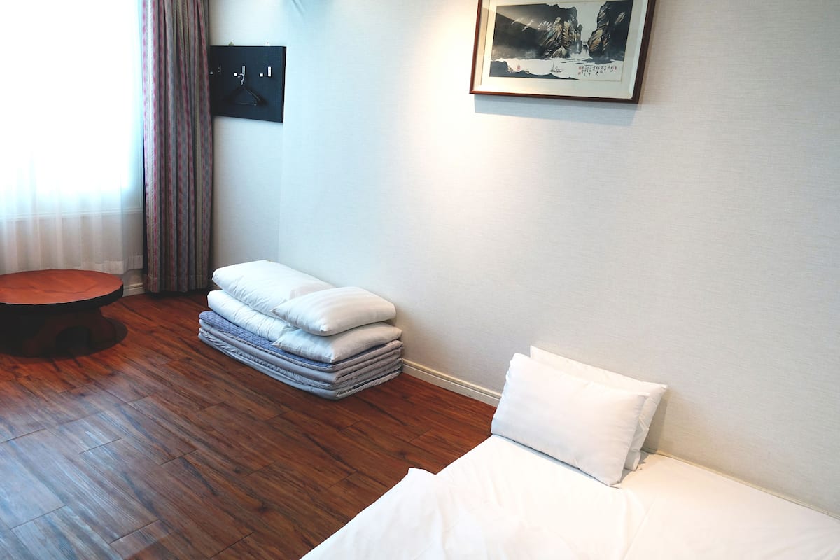 A hotel room with a bed, a round table, and a stack of pillows.