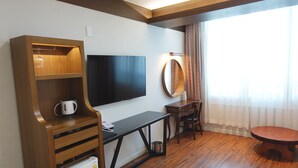 A hotel room with a wooden desk, a flat-screen TV, a small refrigerator, a coffee maker, a dining table, a chair, and a large mirror. - Prince Hotel (Goseong)