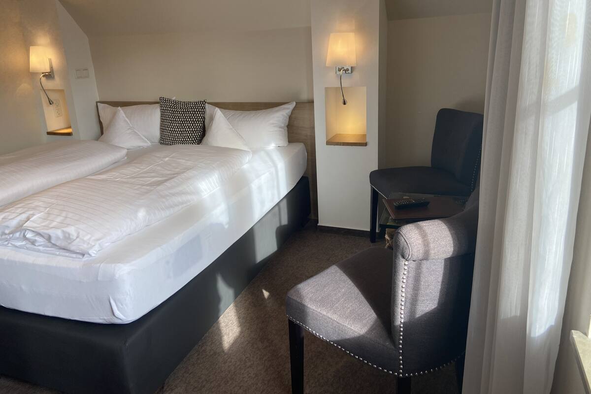 A hotel room with a double bed, a small desk, a chair, and two wall-mounted lamps.