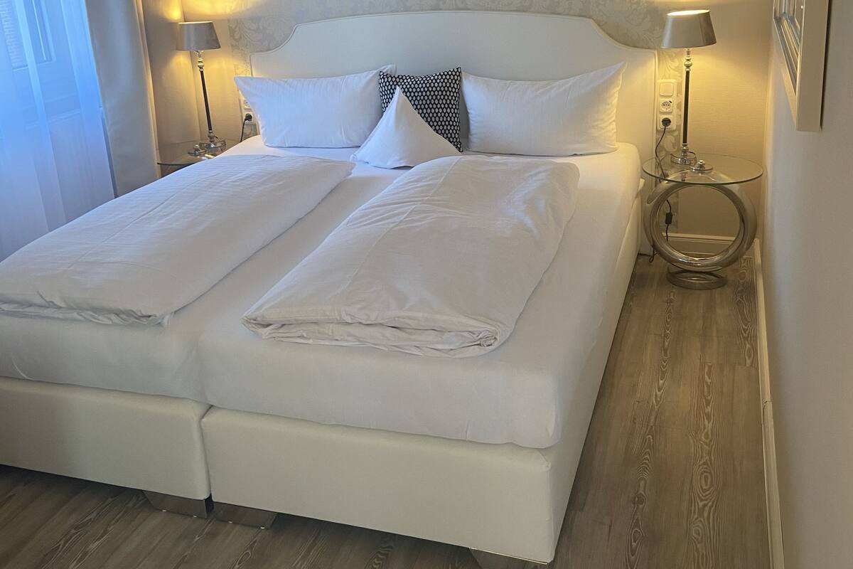 A neatly made bed with white linens, two bedside lamps, and a patterned wallpaper headboard.