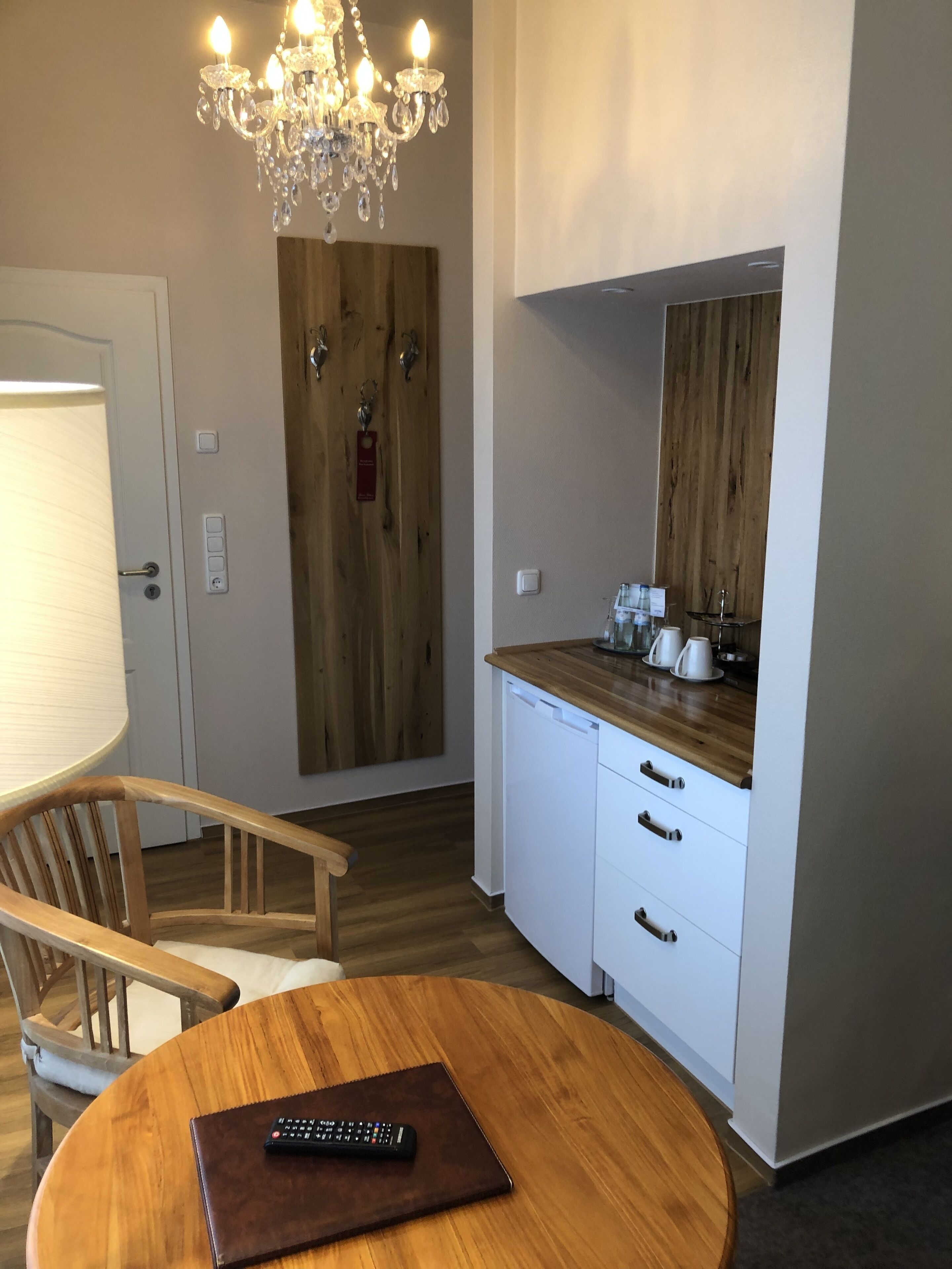 A modern kitchen with a wooden countertop, white cabinets, a chandelier, and a dining area with a chair and a remote control on the table.