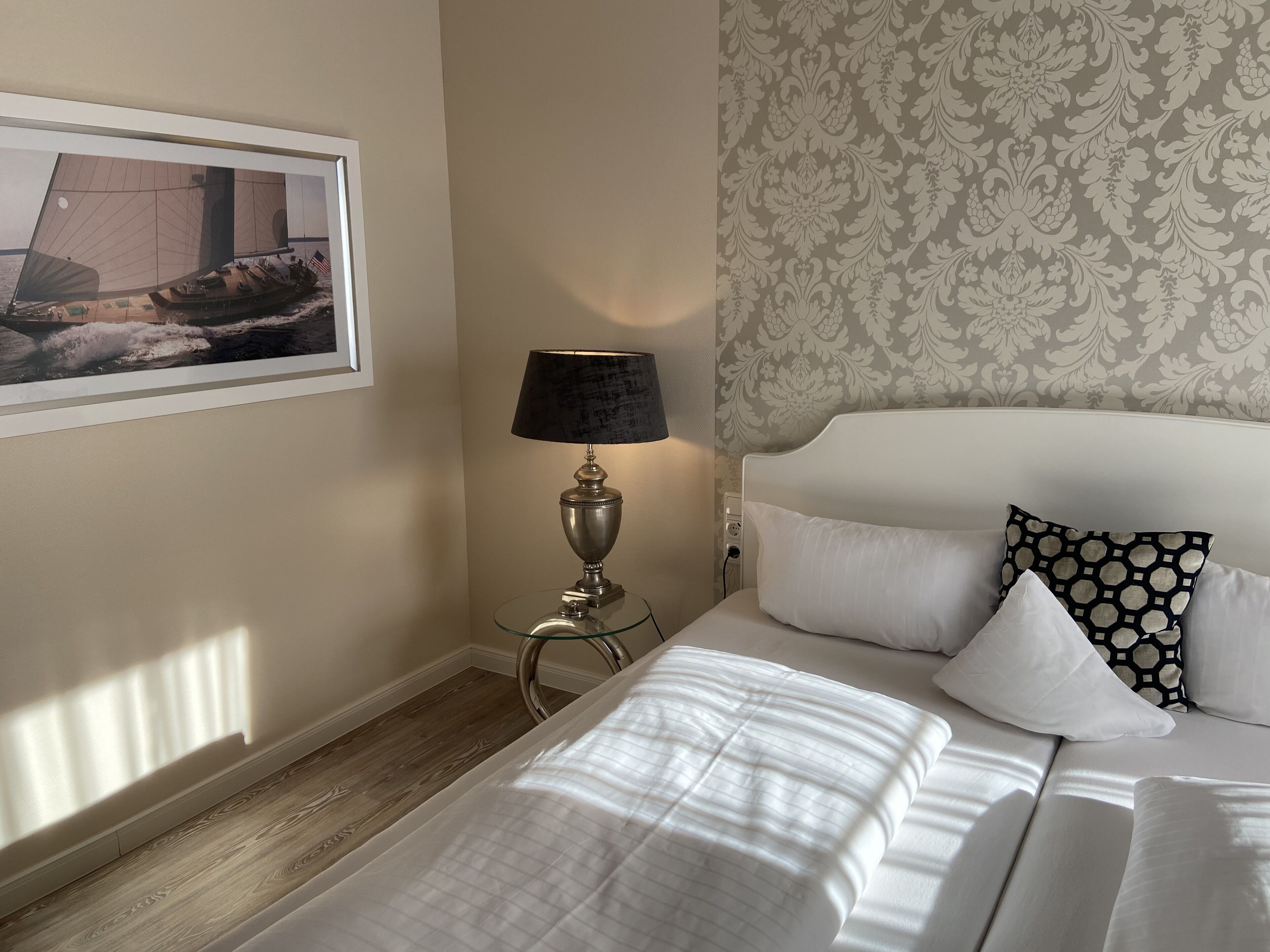 A neatly made bed with white linens, a bedside lamp, and a framed picture on the wall.