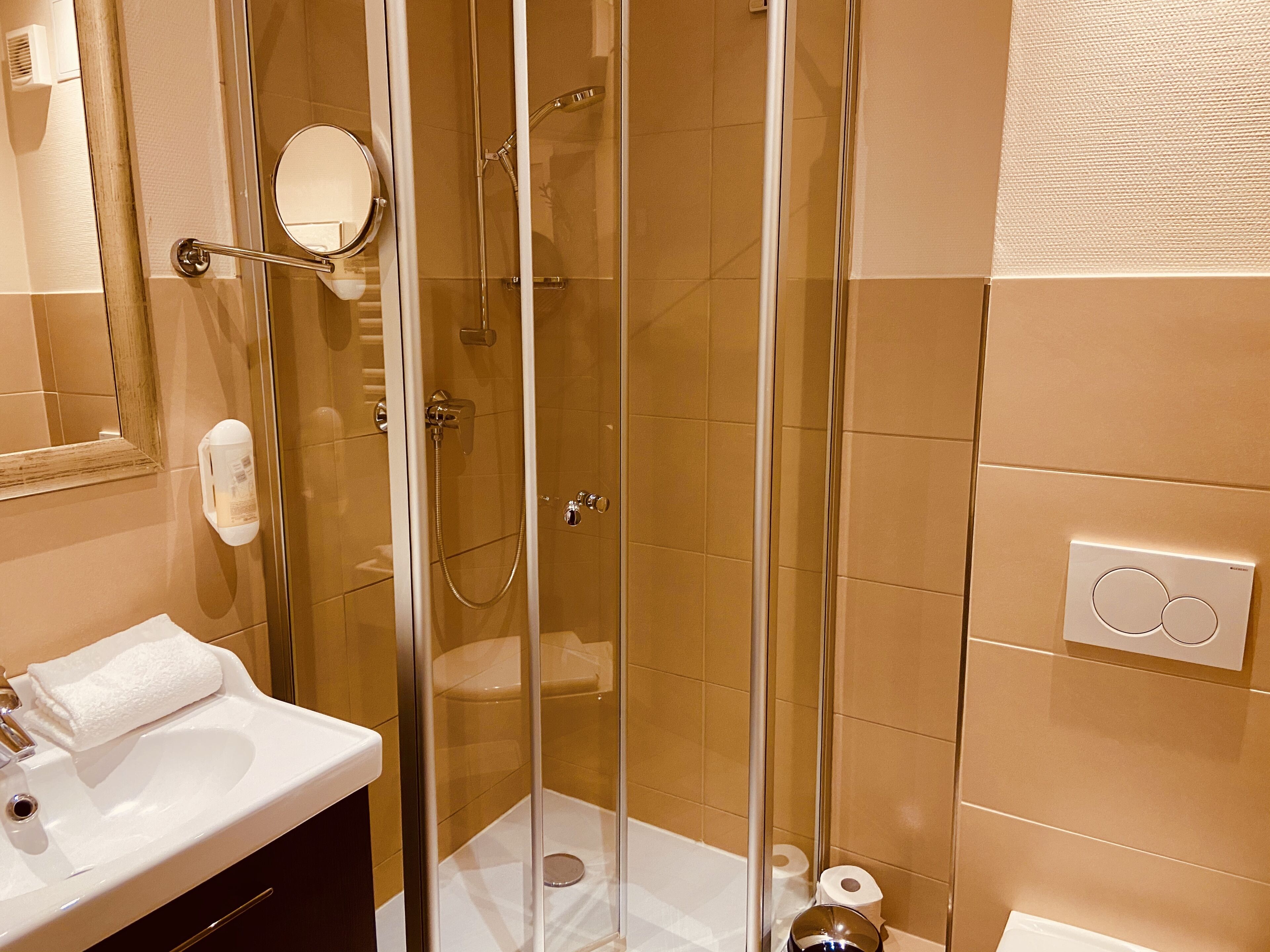 A glass-enclosed shower with a handheld showerhead, a white sink with a towel, and a mirror.