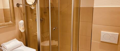 A glass-enclosed shower with a handheld showerhead, a white sink with a towel, and a mirror.