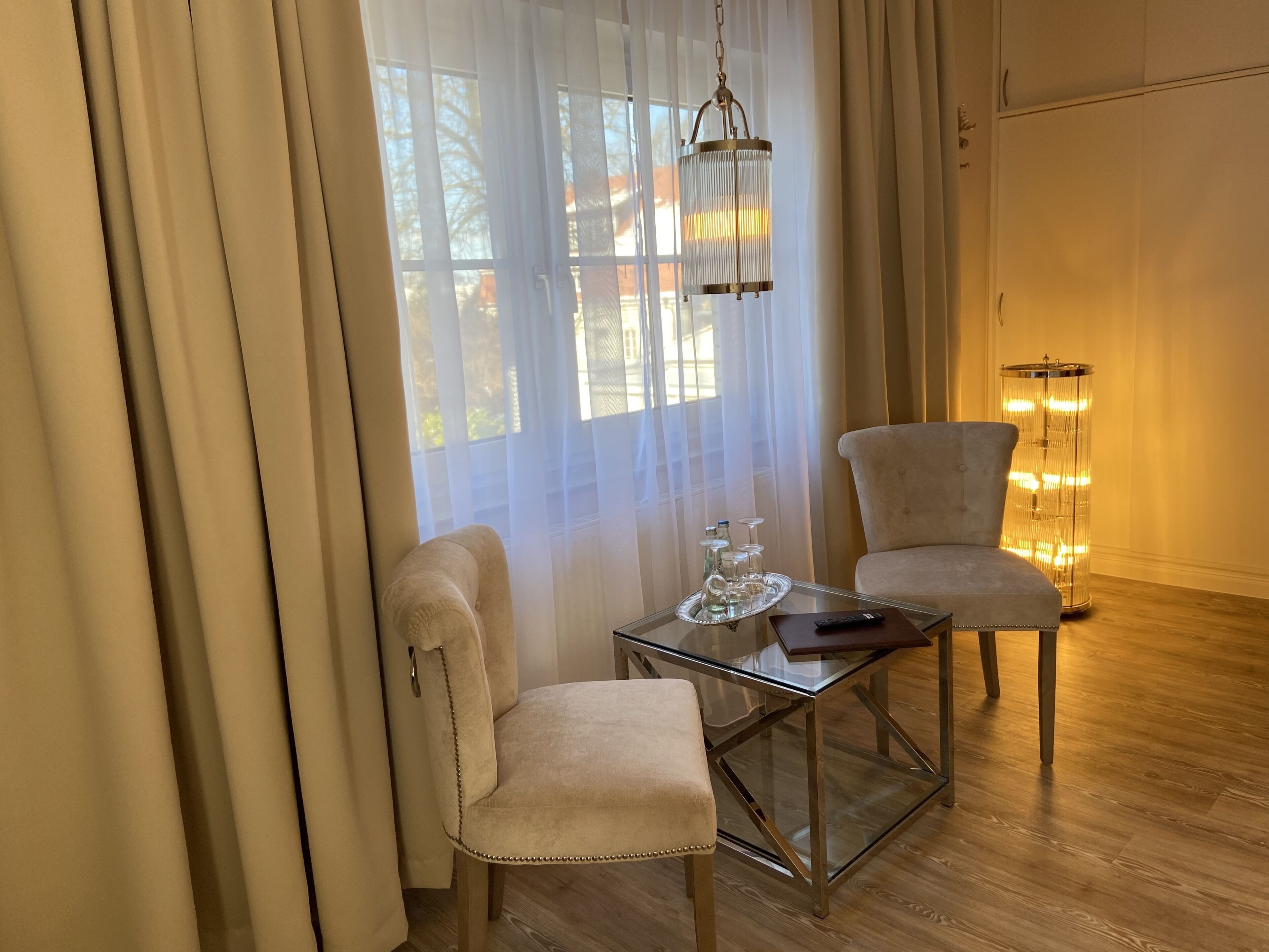 Een kamer met twee stoelen, een glazen bijzettafeltje, een hanglamp en een hoge staande lamp.