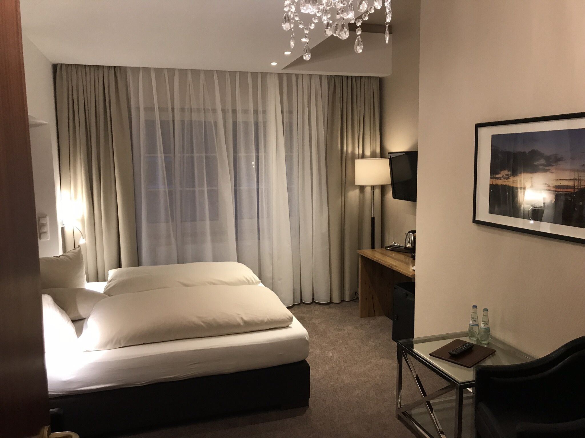 Una habitación de hotel con una cama, un escritorio, una silla, un televisor, una lámpara y un cuadro en la pared.