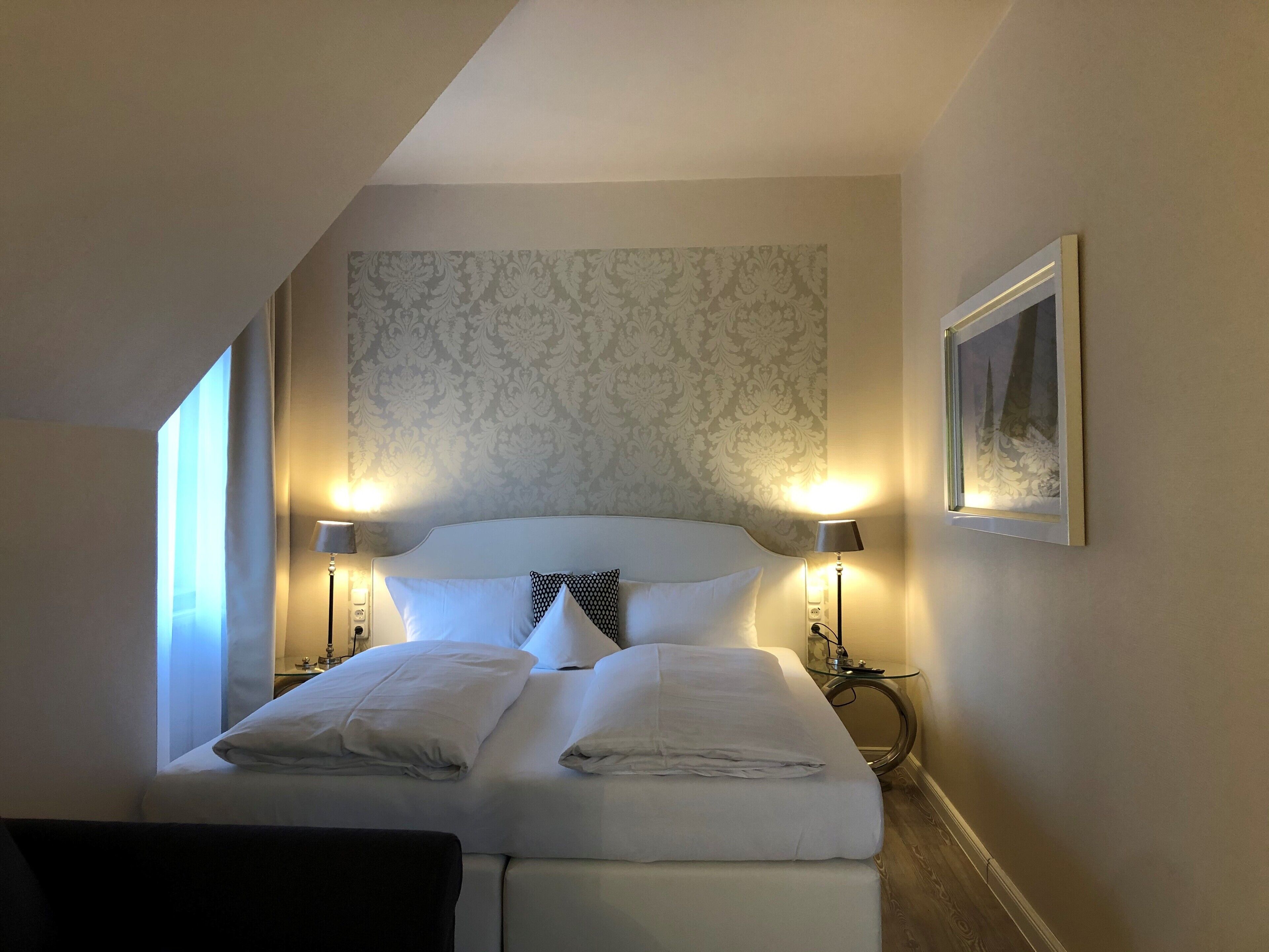 Ein Hotelzimmer mit einem Bett, zwei Nachttischlampen, einem Nachttisch und einem gerahmten Bild an der Wand.