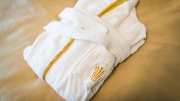 Een witte handdoek met gouden bies en een gevlochten gouden handgreep, netjes gevouwen op een bed.