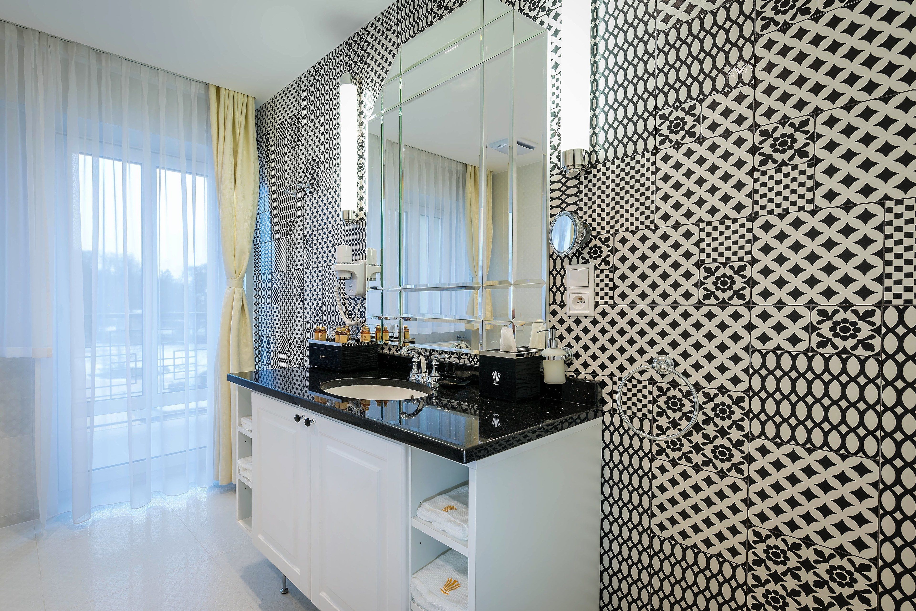 A modern bathroom with a black countertop sink, a large mirror, and patterned walls.