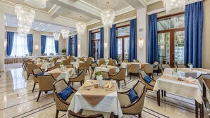 Uma sala de jantar formal com várias mesas, cadeiras e lustres.