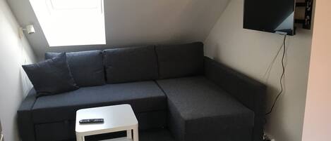 A modern living room with a grey sectional sofa, a small white side table, and a mounted flat-screen TV.