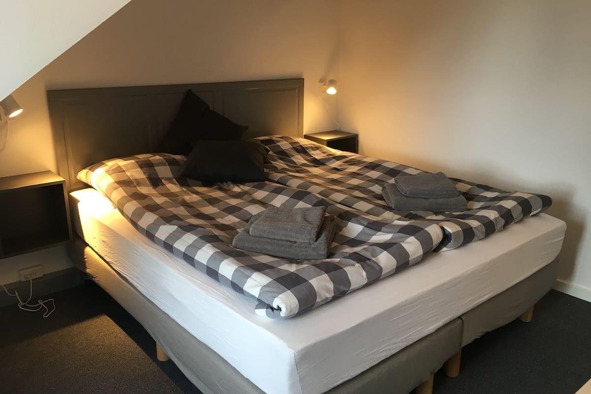 A neatly made bed with a checkered bedspread and pillows, two bedside tables with lamps, and a sloped ceiling.