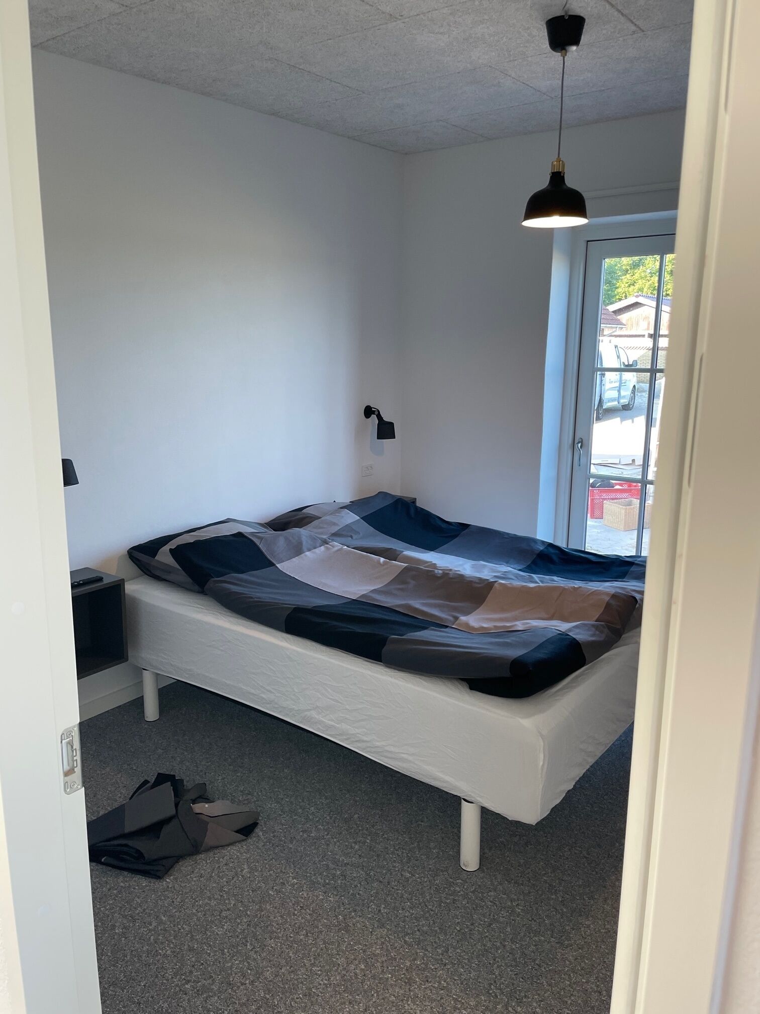 Un dormitorio con una cama, una mesita de noche, una lámpara y un ventanal.
