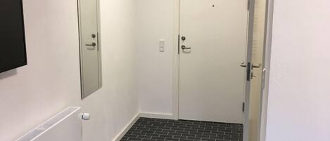 A hallway with two doors, a vent, and a black and white tiled floor.