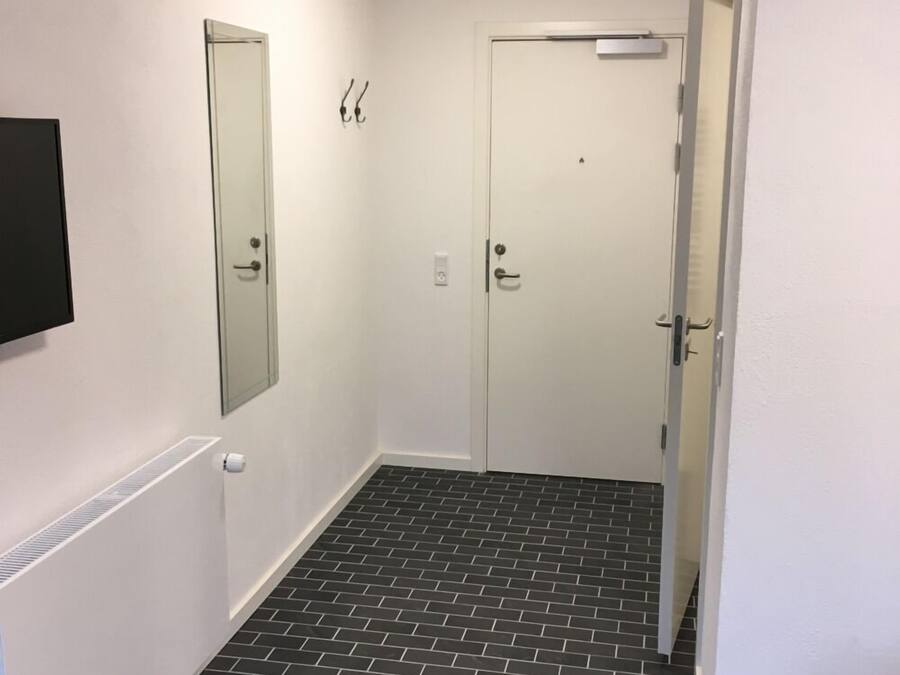 Un pasillo con dos puertas, una rejilla de ventilación y un suelo de baldosas blanco y negro.