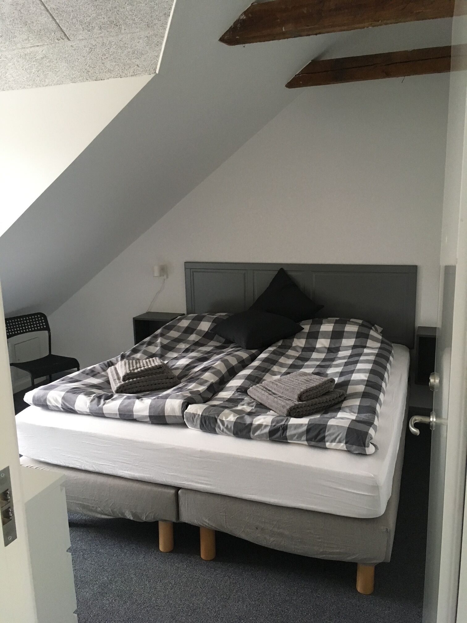 Un dormitorio con colcha a cuadros, colchón gris y cabecera de madera.