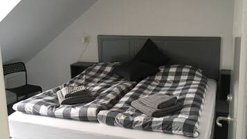 A bedroom with a checkered bedspread, a grey mattress, and a wooden headboard.