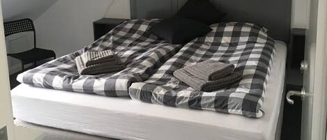 Un dormitorio con colcha a cuadros, colchón gris y cabecera de madera.