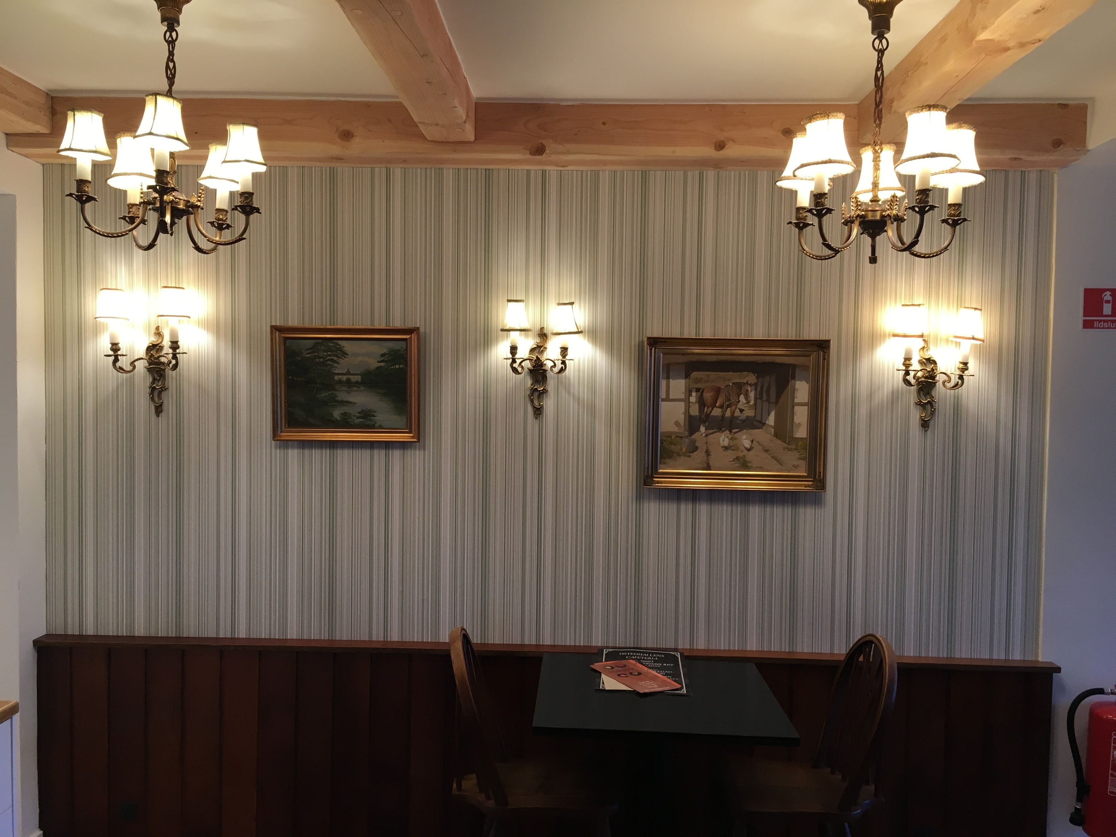 A dining area with wooden paneling, two chandeliers, and two framed paintings on the wall.
