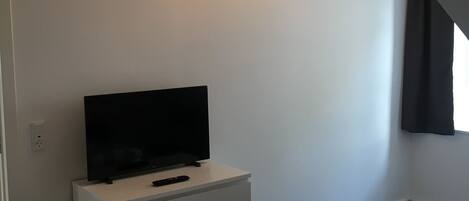 Un dormitorio con una televisión sobre un tocador blanco, una colcha a cuadros y una lámpara colgante.