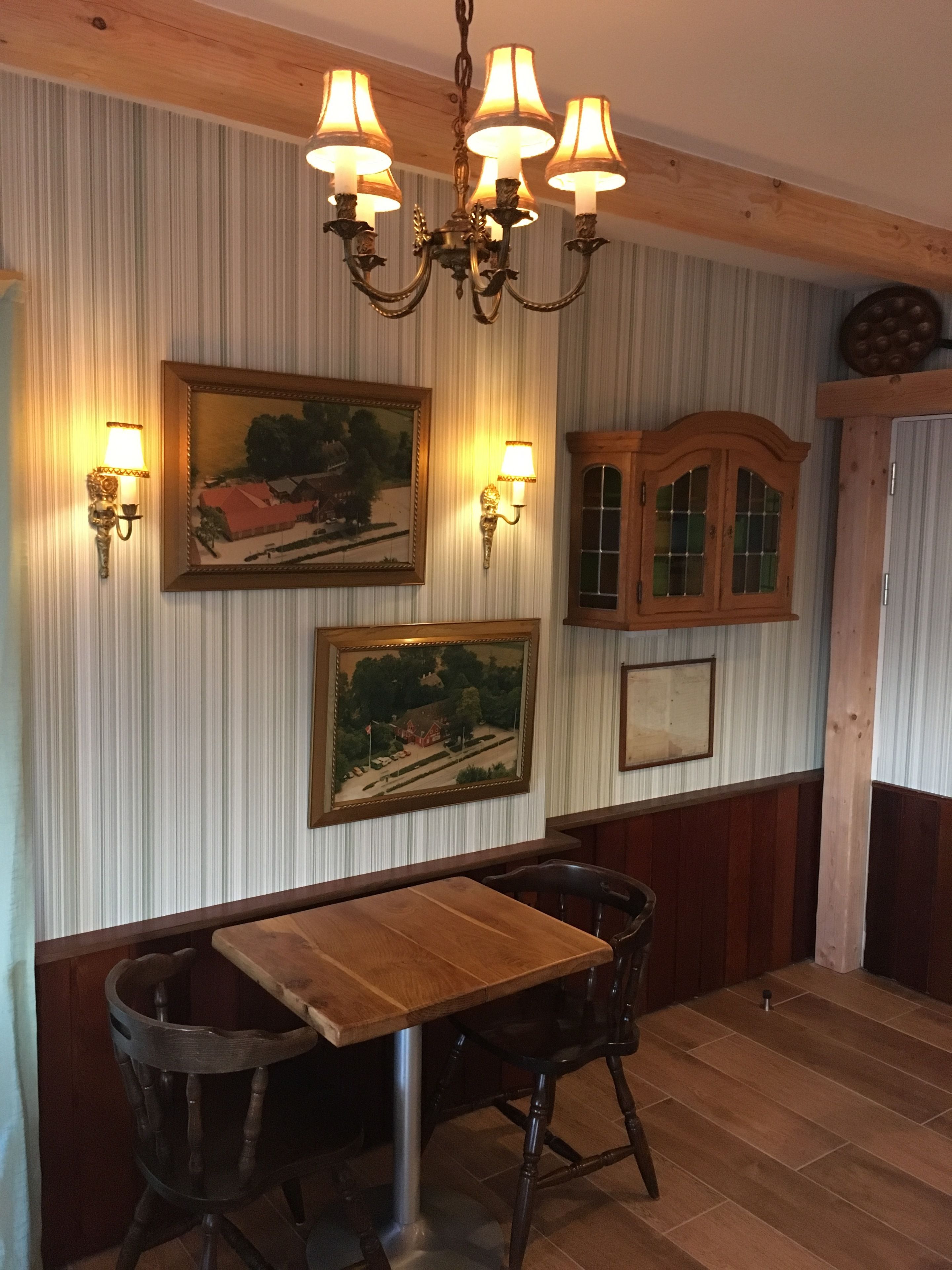 Un comedor con una mesa y sillas de madera, una araña y dos lámparas de pared.