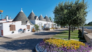 A row of white buildings with conical roofs, a bicycle, and a flower bed with the text "BED & BREAKFAST". - Trulli San Leonardo (Alberobello)