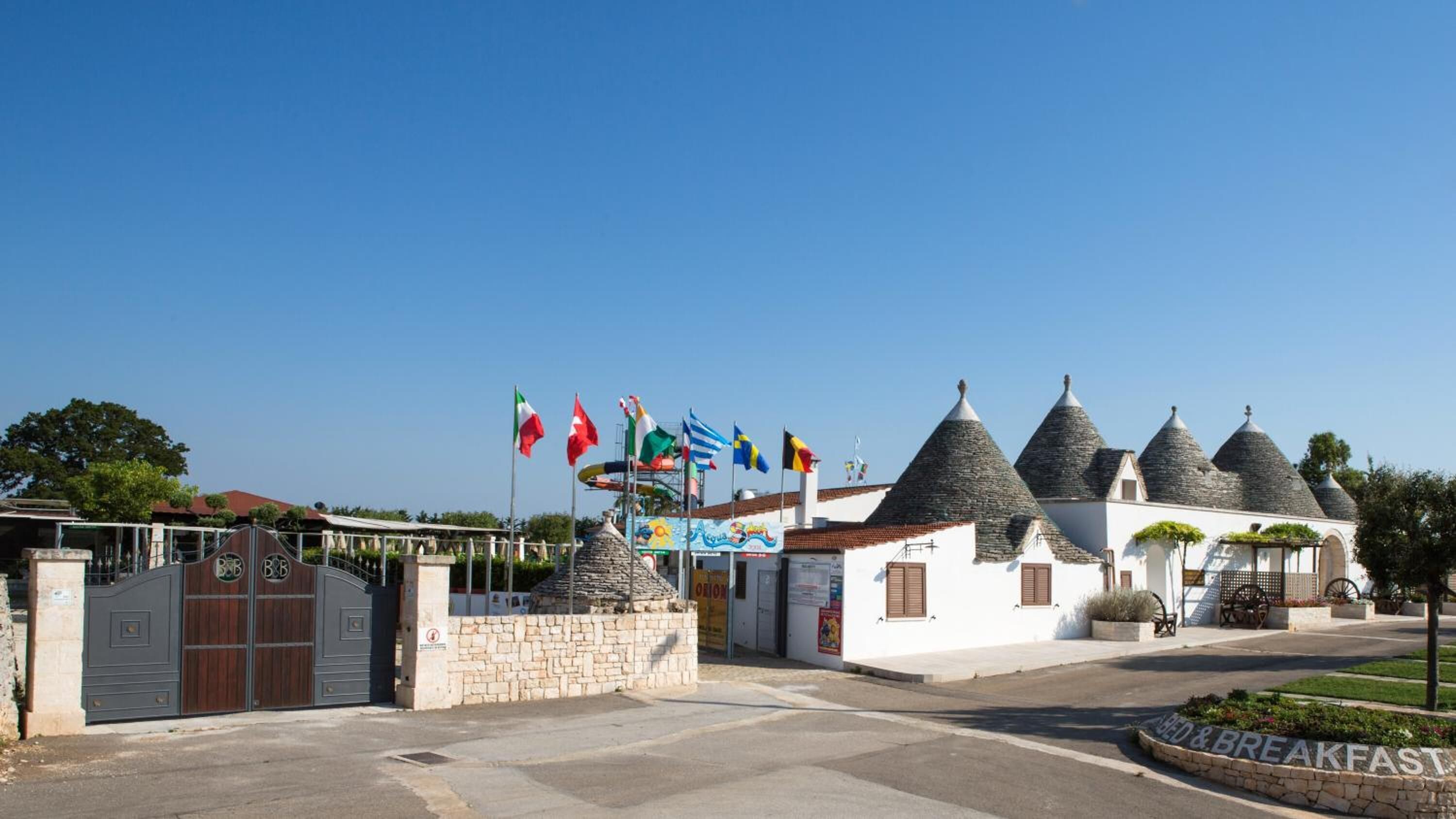 Un edificio con techos cónicos, una entrada de muro de piedra y varias banderas.