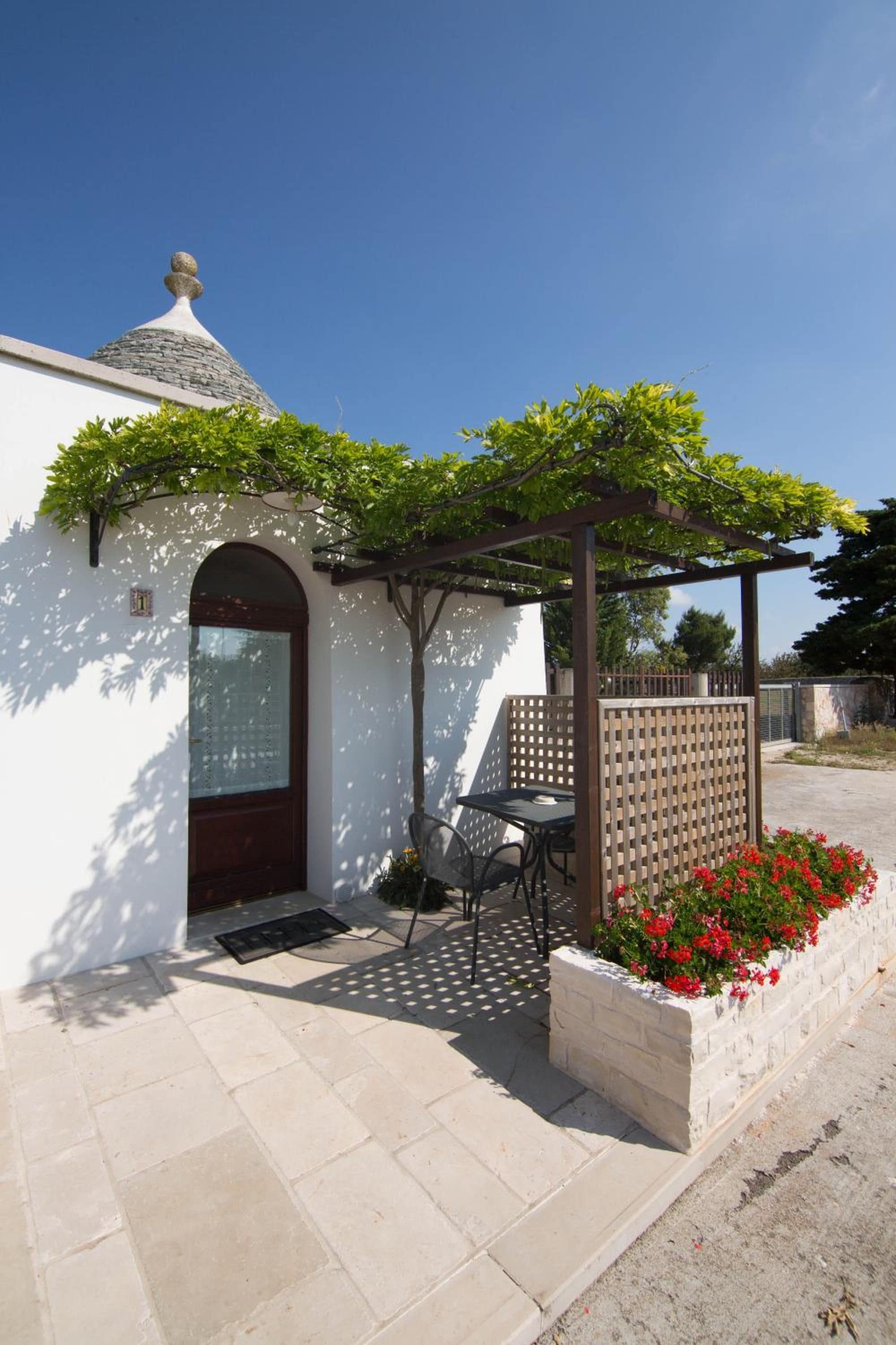 A small building with a white exterior, a dark door, and a small porch area with a table and chairs.