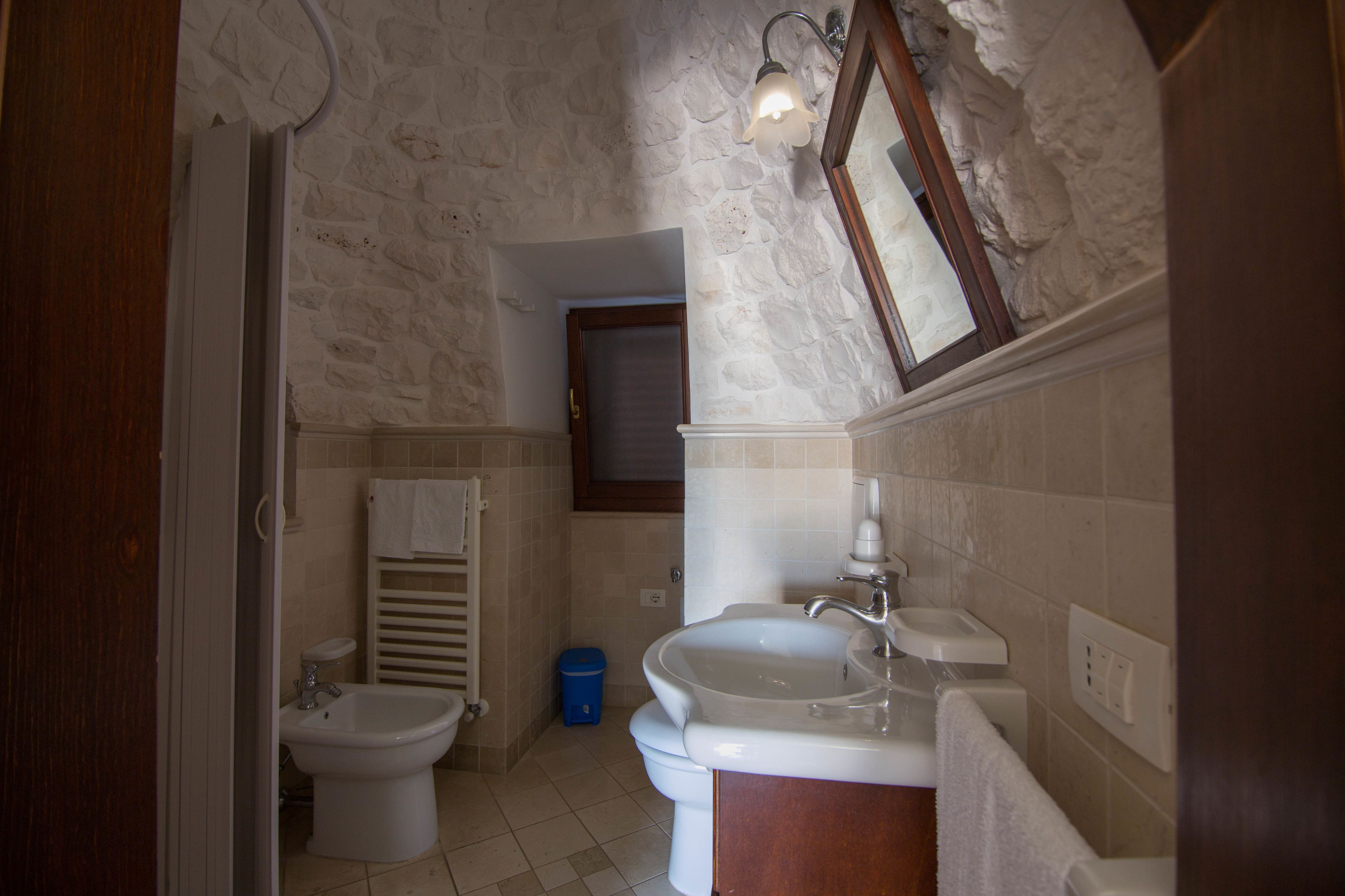 A bathroom with a stone wall, a bidet, a sink, and a mirror.