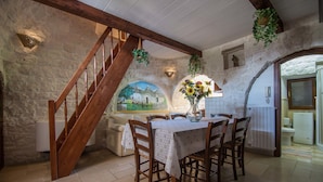 A rustic dining area with a wooden staircase, stone walls, and a mural. - Trulli San Leonardo (Alberobello)