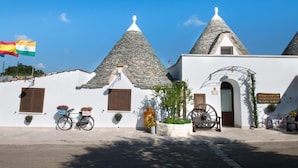 A traditional building with conical roofs, a white facade, and a signboard. - Trulli San Leonardo (Alberobello)