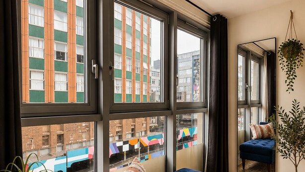 A room with a blue sofa, a round table with a plant, and large windows with a view of buildings. - Lovely Bohemian Apartment in Heart of City Life (Glasgow)