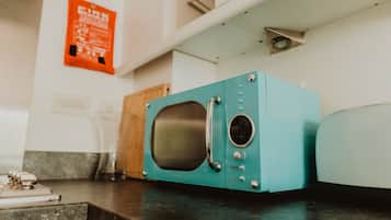 Un microondas color turquesa sobre una encimera de cocina con un mueble de madera y un vaso al fondo.