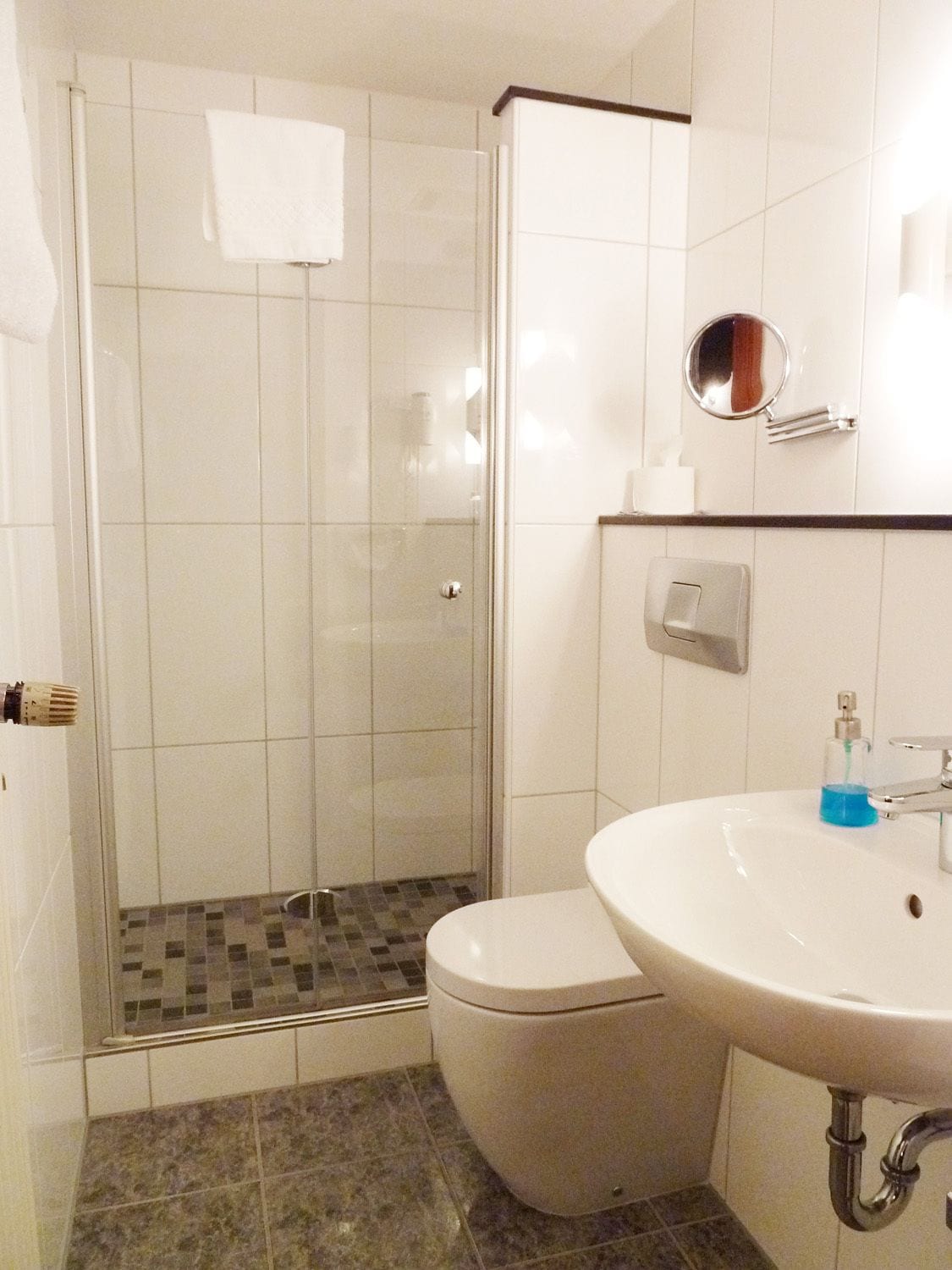 A bathroom with a shower, toilet, sink, and a mirror.