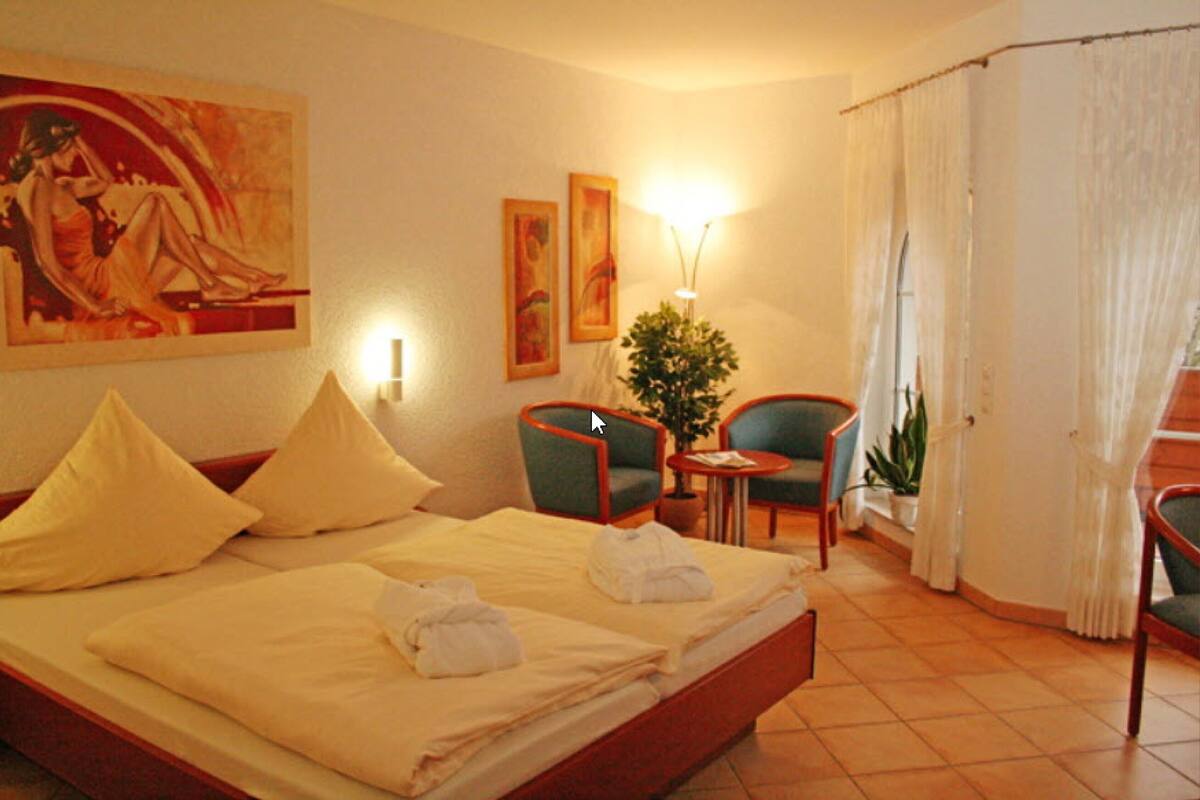 Habitación de hotel con cama, dos sillas, una mesa, lámpara y obras de arte en las paredes.