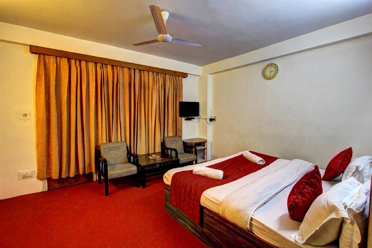 A hotel room with a bed, a desk, a chair, a television, and a ceiling fan.