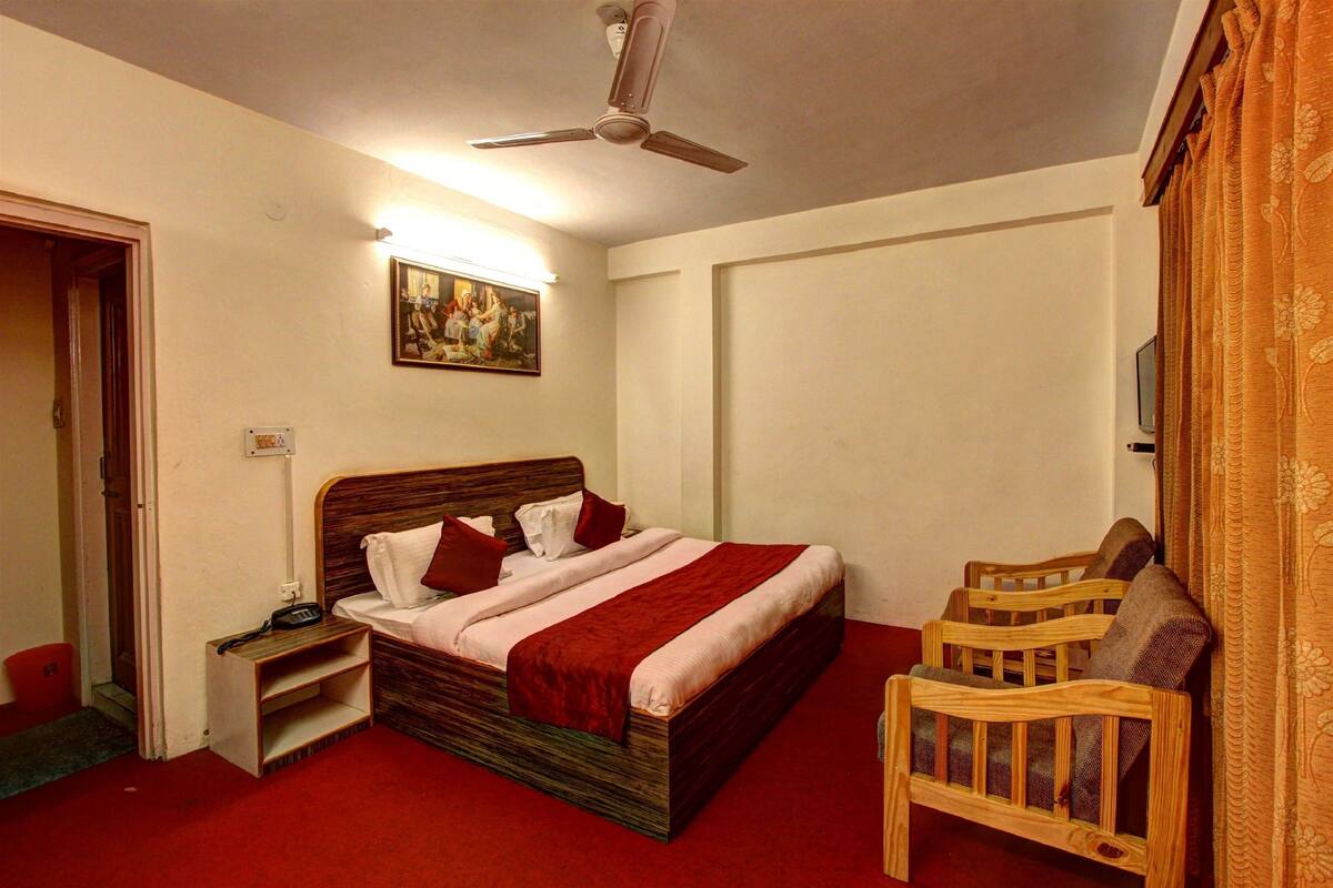 A bedroom with a bed, a nightstand, a wooden chair, a ceiling fan, and a painting on the wall.