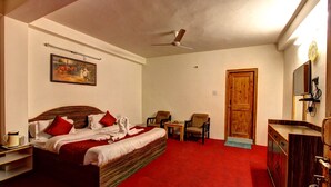 A bedroom with a bed, a desk, a chair, a wooden door, and a ceiling fan. - Hotel Monarch Residency (Manali)