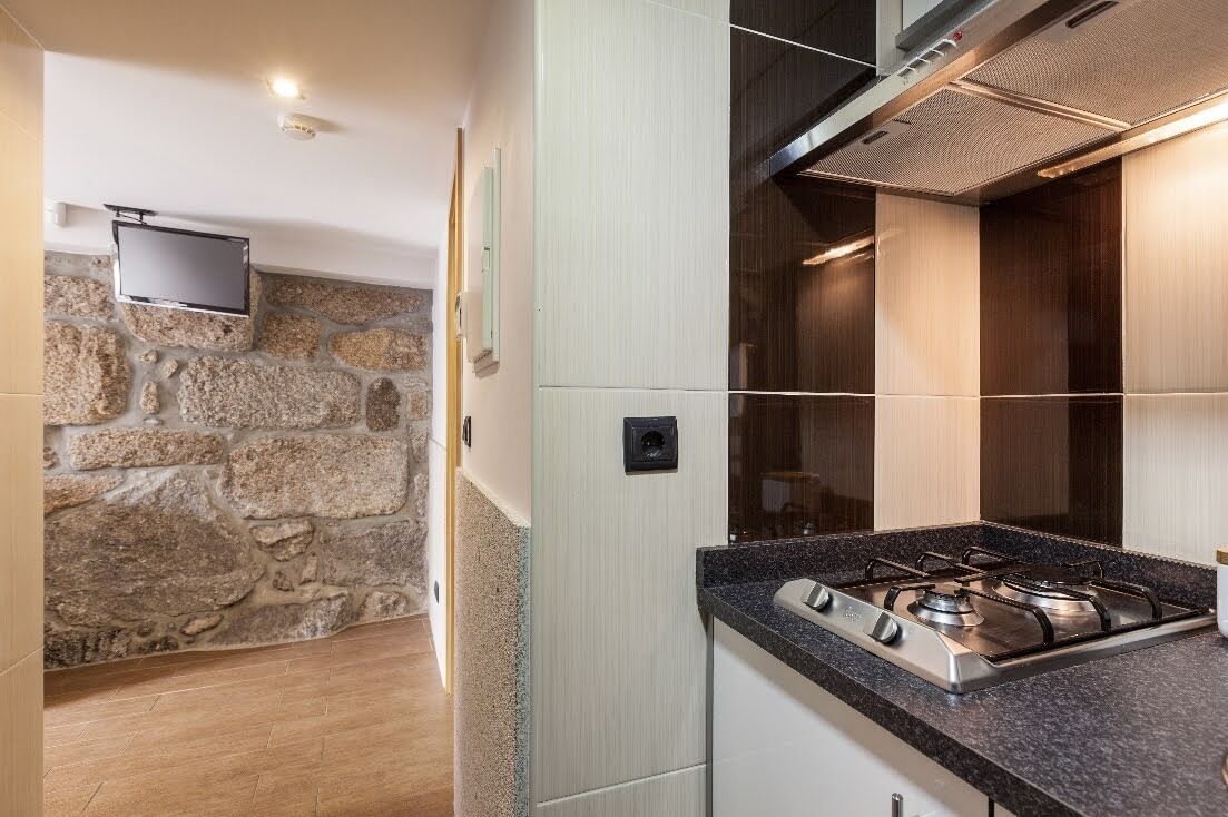 Una cocina moderna con una pared de acento de piedra, una estufa a gas empotrada y un televisor de pantalla plana montado en la pared.