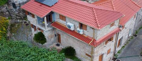 A stone building with a red-tiled roof, solar panels, and air conditioning units.