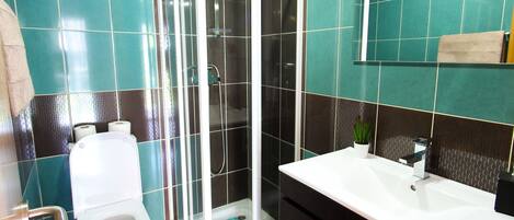 A bathroom with a toilet, a shower enclosure, and a sink with a mirror.