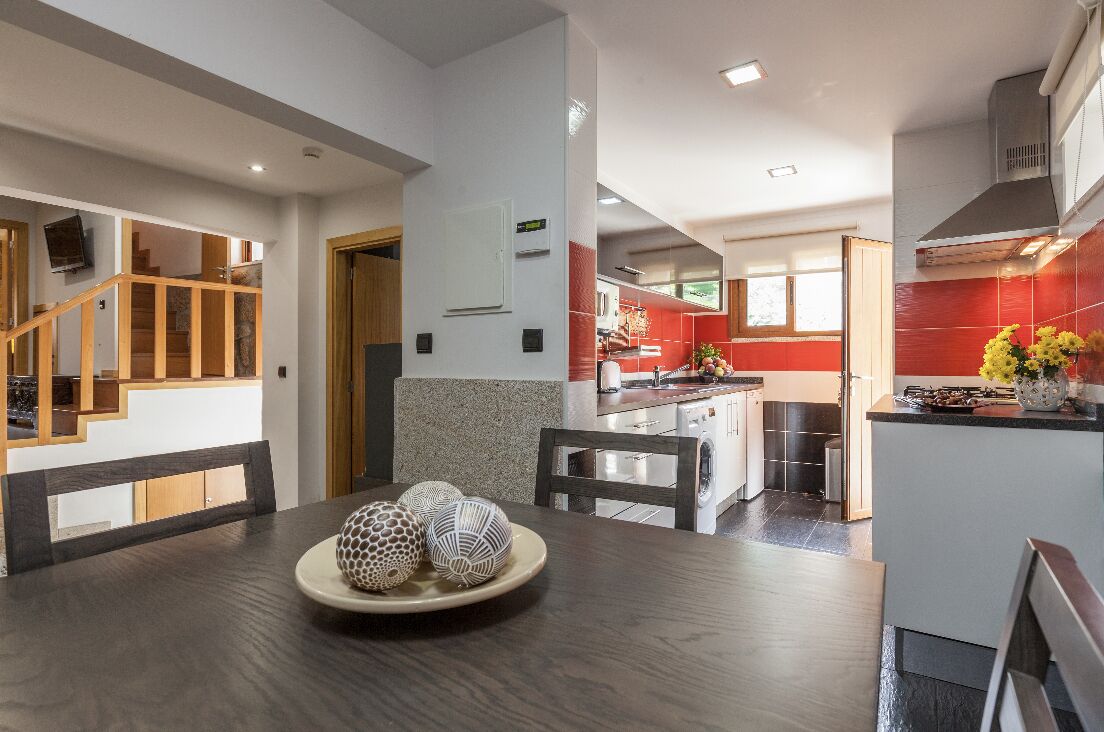 A modern kitchen with red tiles, a dining area with a wooden table, and a staircase leading to an upper level.