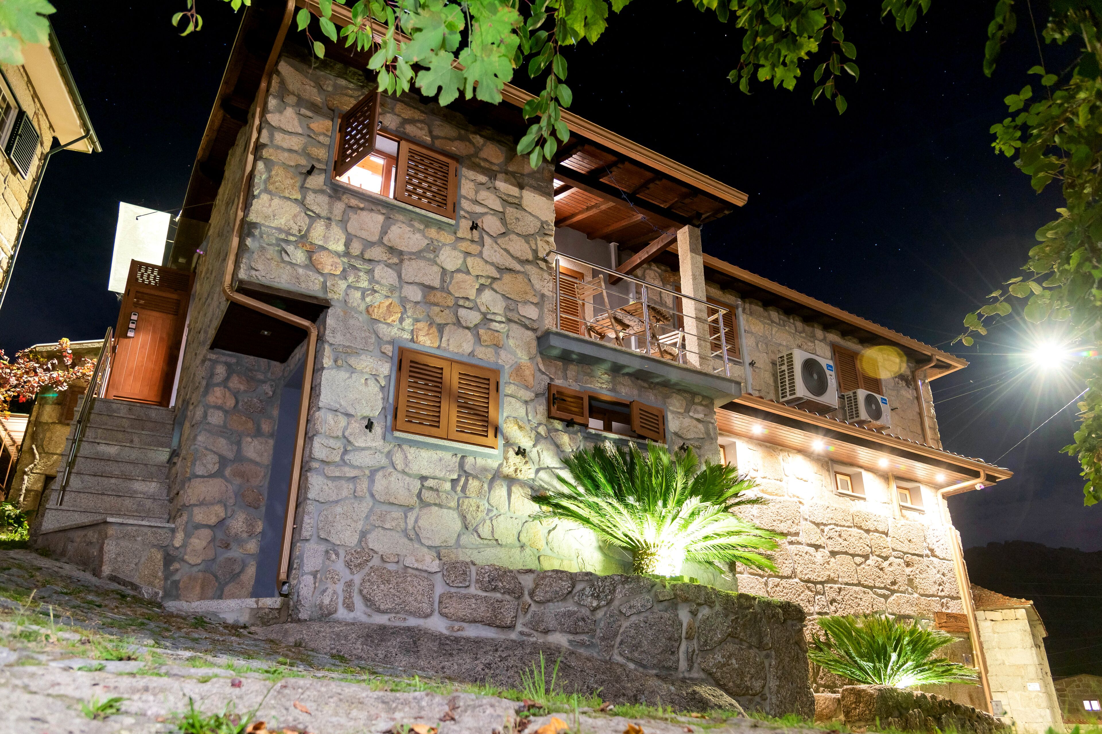Um edifício de pedra com varanda, persianas de madeira e aparelhos de ar condicionado.