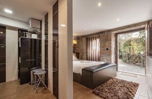 A modern bedroom with a large bed, a small seating area, and a view of the outdoors. - Casa da fonte (Terras de Bouro)
