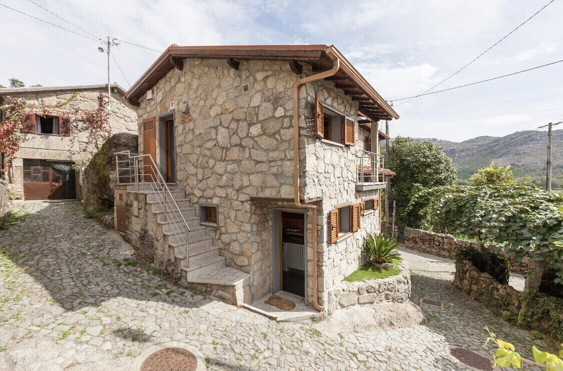 A stone house with a wooden staircase leading to a balcony.