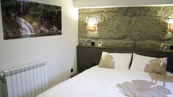 Un dormitorio con una cama grande, una pared de piedra, un cuadro con una cascada y un radiador.