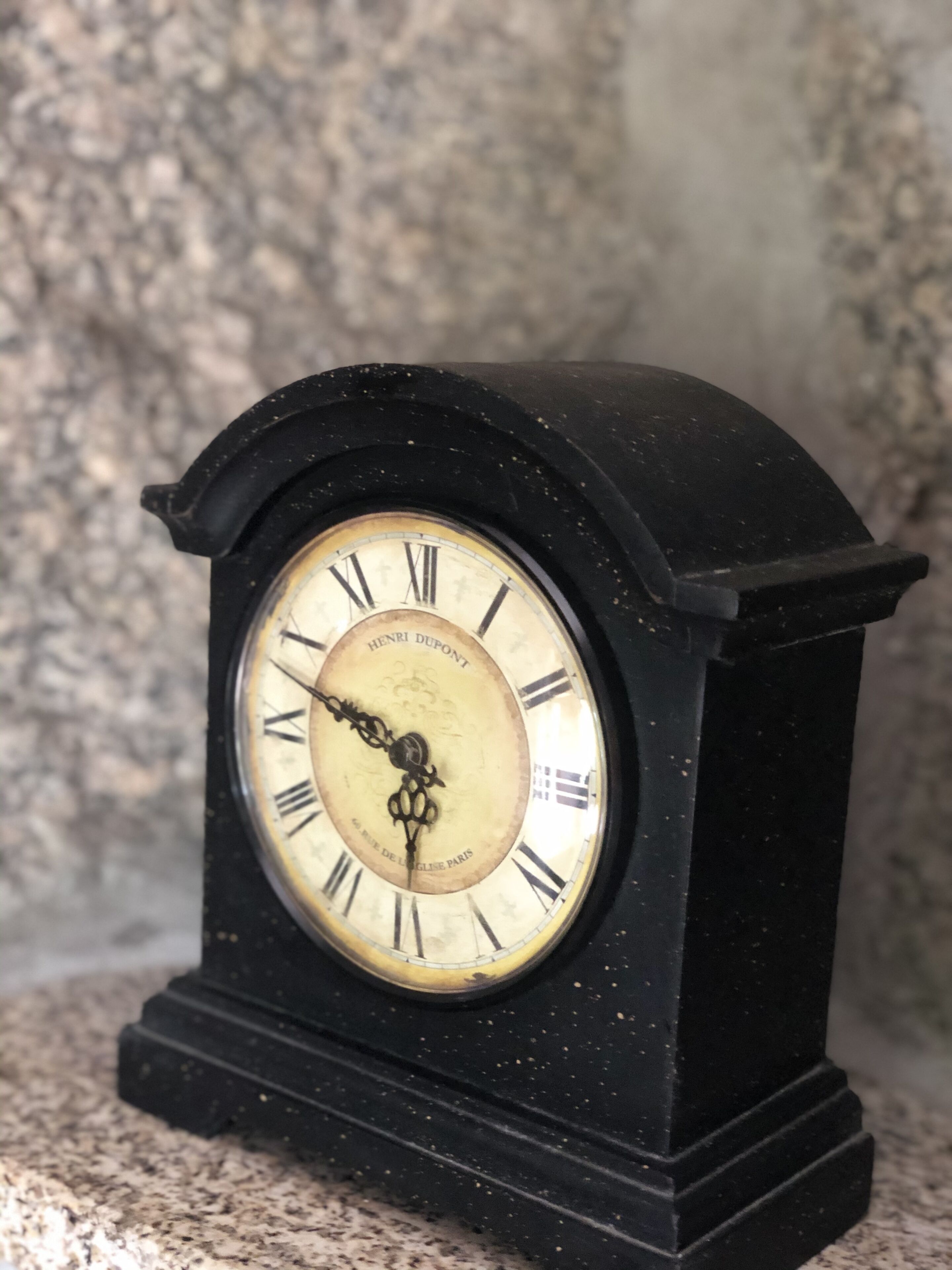 A vintage black clock with Roman numerals and a brand name on its face.