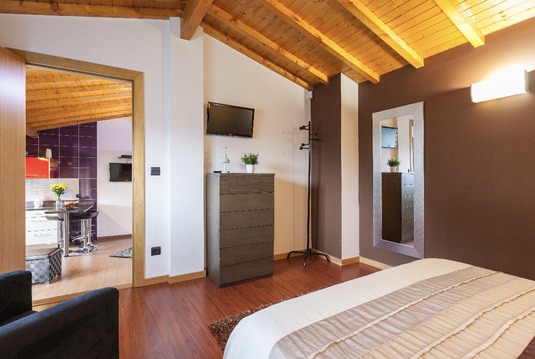 A bedroom with a bed, wooden ceiling, a TV, a dresser, and a mirror.