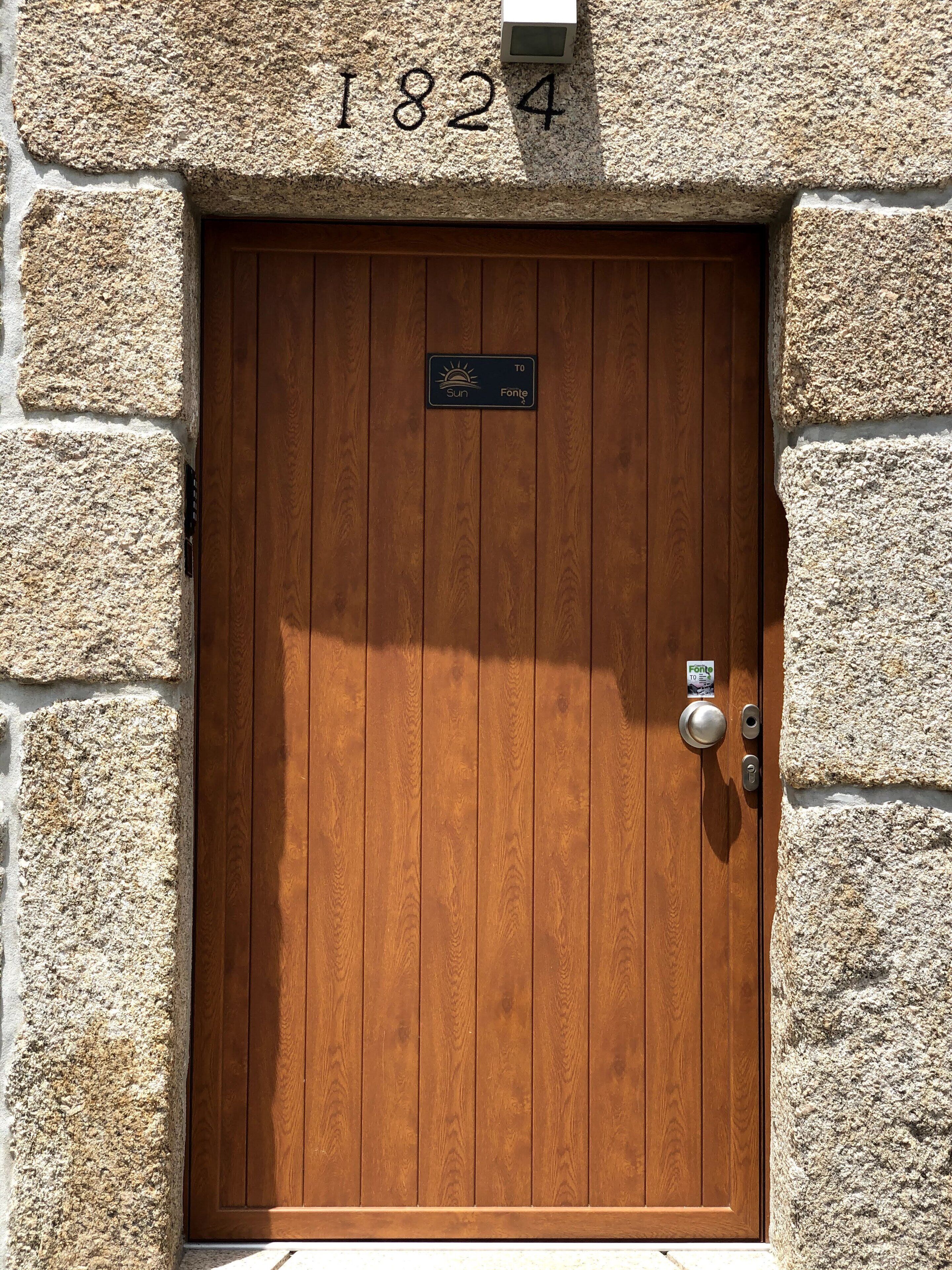 A wooden door with a stone wall, a number plaque, and a weather sign.